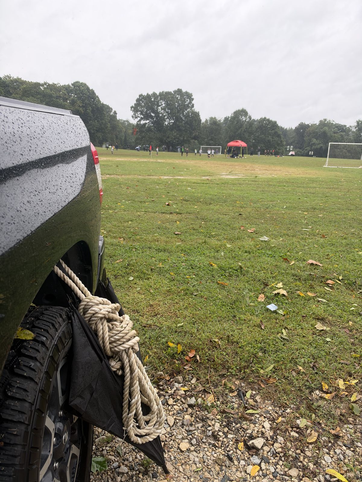 The loose coil hung on the truck's mud flap beside the soccer field
