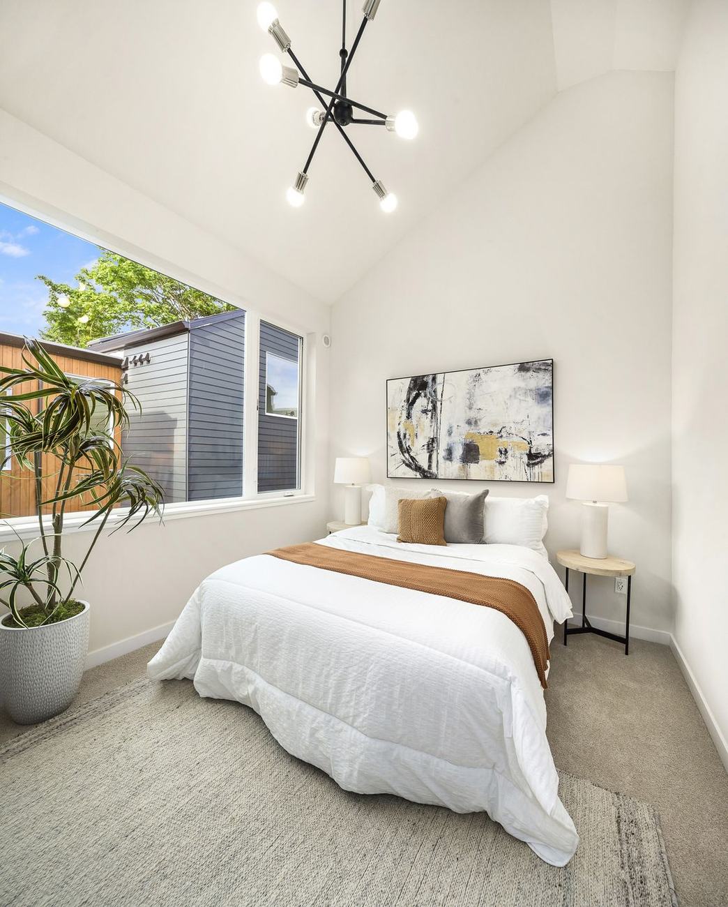 Vaulted bedroom with a large window onto trees and a sputnik light