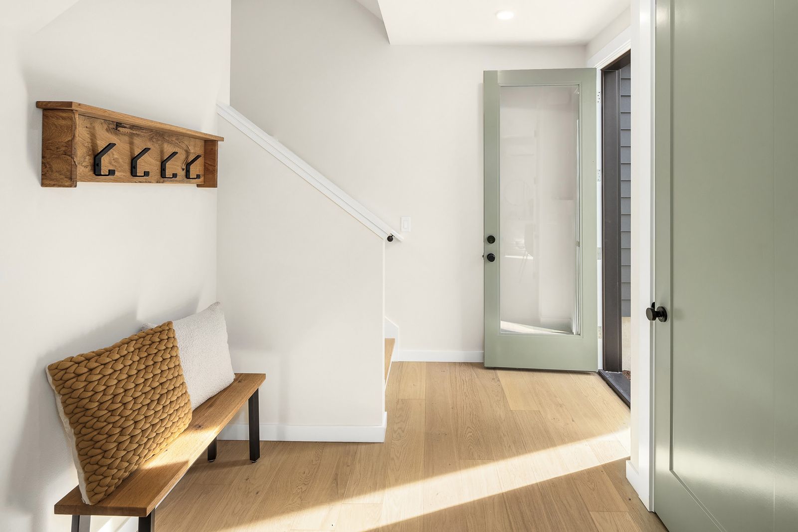 Entry hall with a wooden bench, wall hooks, white oak floor and a sage door