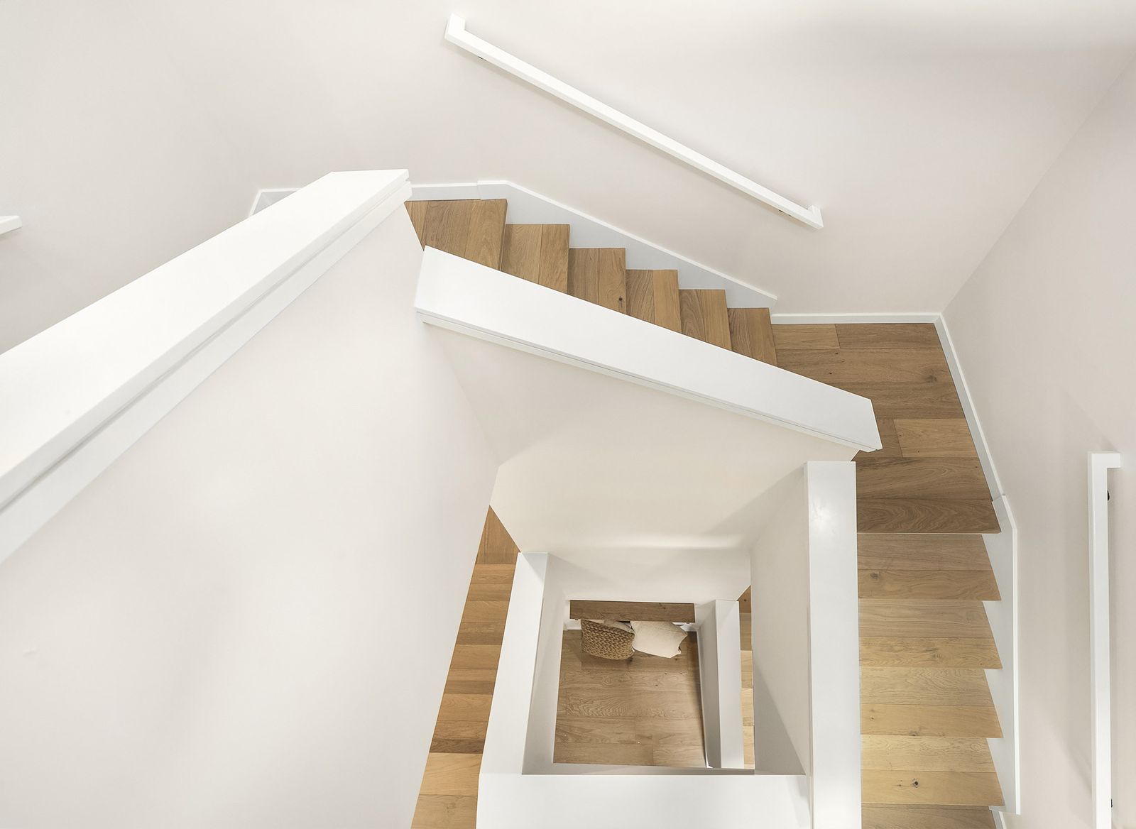 Looking down an open white stair with oak treads through three floors