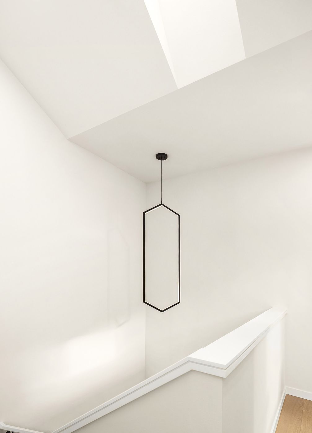 White stairwell lit from a skylight above, with a thin black pendant light