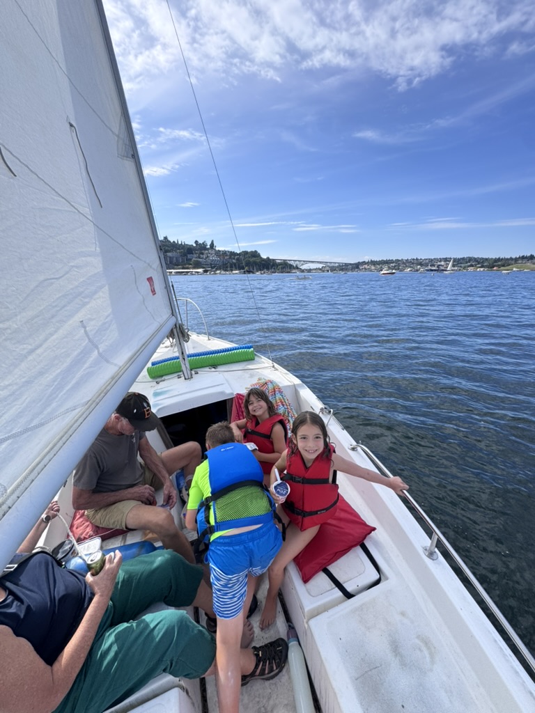 Grandparents and three children in life jackets filling the cockpit under sail.