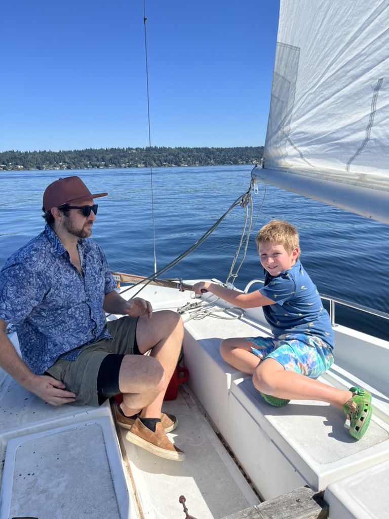 Will and a young Wiley sitting in the cockpit under sail on a bright day.